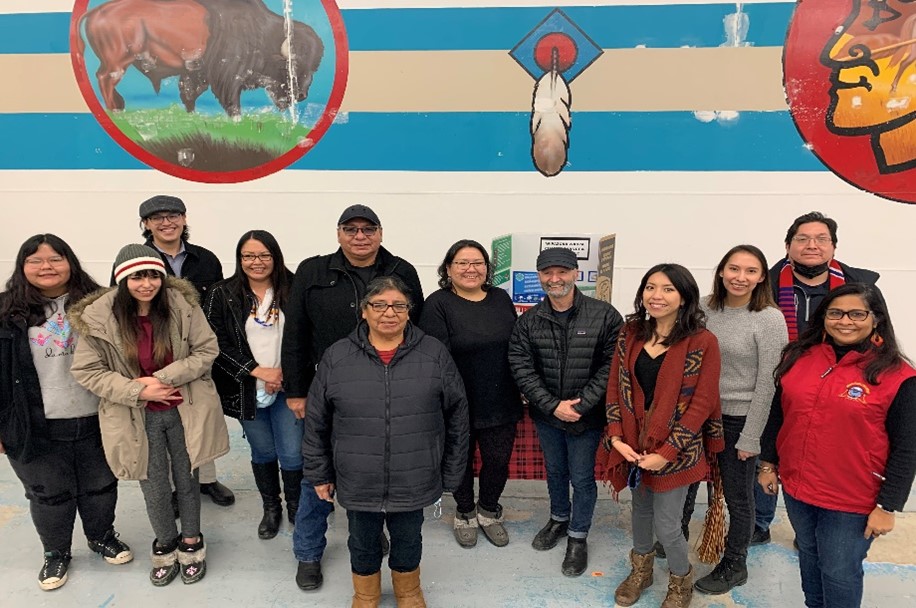 11 people standing together against a wall painted with Indigenous art