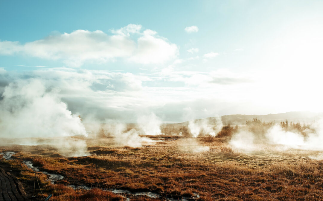 Exhaust from underground geothermal energy is rising to the surface of a field. It looks like there are clouds sitting on top of various parts of the field.